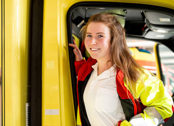 Eine Notfallsanitäterin steht am Fahrzeug und lächelt in die Kamera.