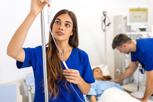 Bild vergr&ouml;&szlig;ern: Eine Krankenschwester richtet eine Infusion, während medizinisches Personal eine Patientin betreut.