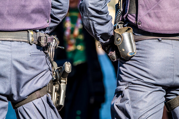 Bild vergr&ouml;&szlig;ern: Nahaufnahme der Dienstg�rtel von zwei Einsatzkr�ften der Bundespolizei in dunkelblauen Uniformen von hinten. Am G�rtel der linken Person ist eine Dienstpistole im Beinhohlster zu sehen, rechts eine Ausr�stungstasche und ein Funkger�t.